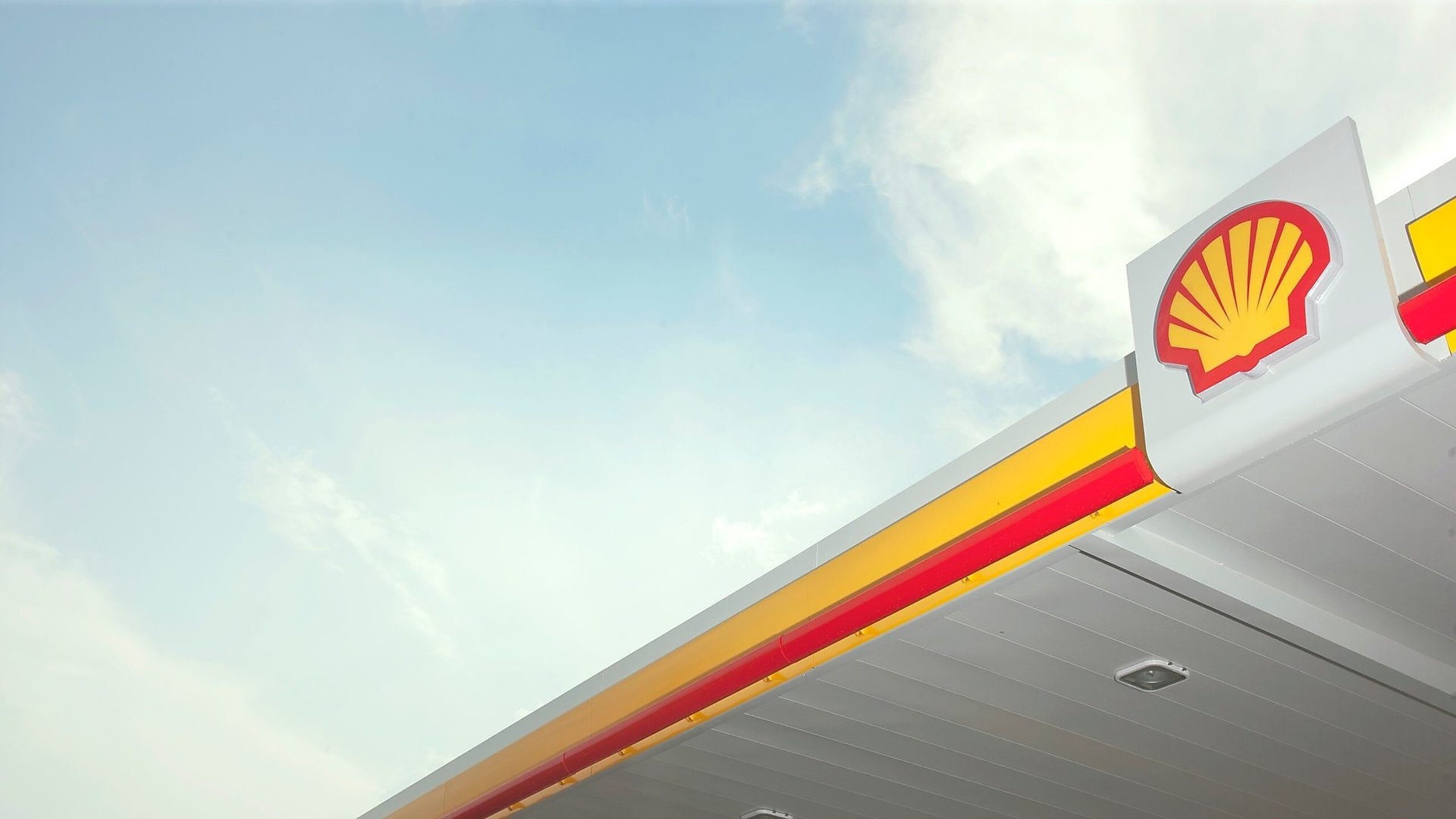 Cobertura de posto de gasolina Shell com o icônico logotipo amarelo e vermelho sob um céu azul claro.
